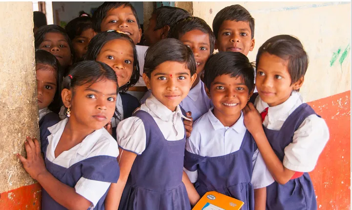 A group of smiling schoolchildren in uniform gathered in a doorway.