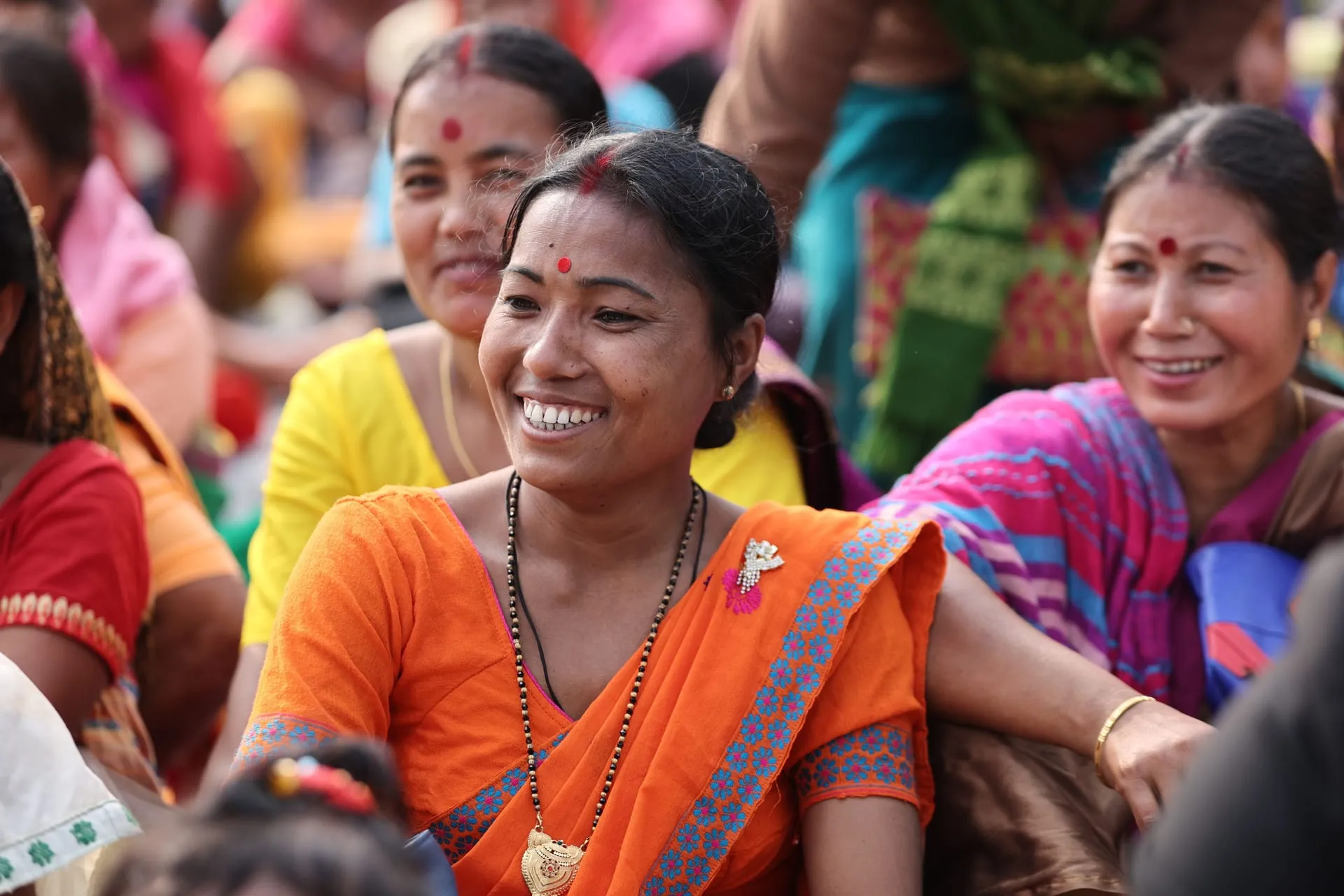 Smiling women in bright saris sitting together at a community gathering.