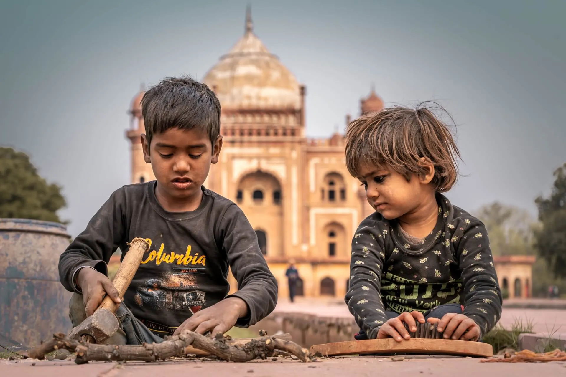 Two children in Delhi, one working with a wooden stick.