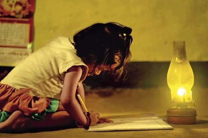A young girl leaning over an open book beside a glowing lamp.