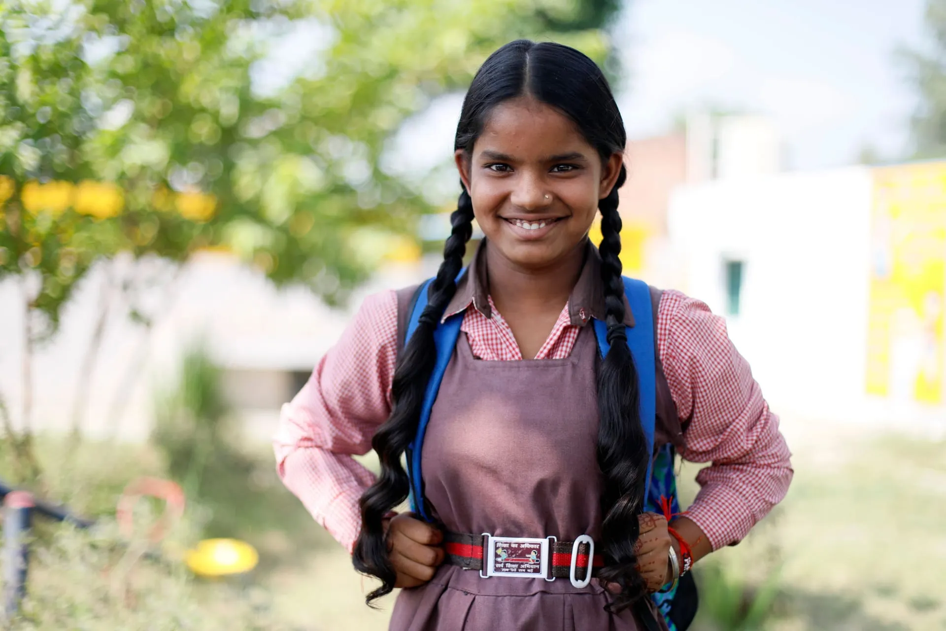A smiling schoolgirl in uniform with her school bag.