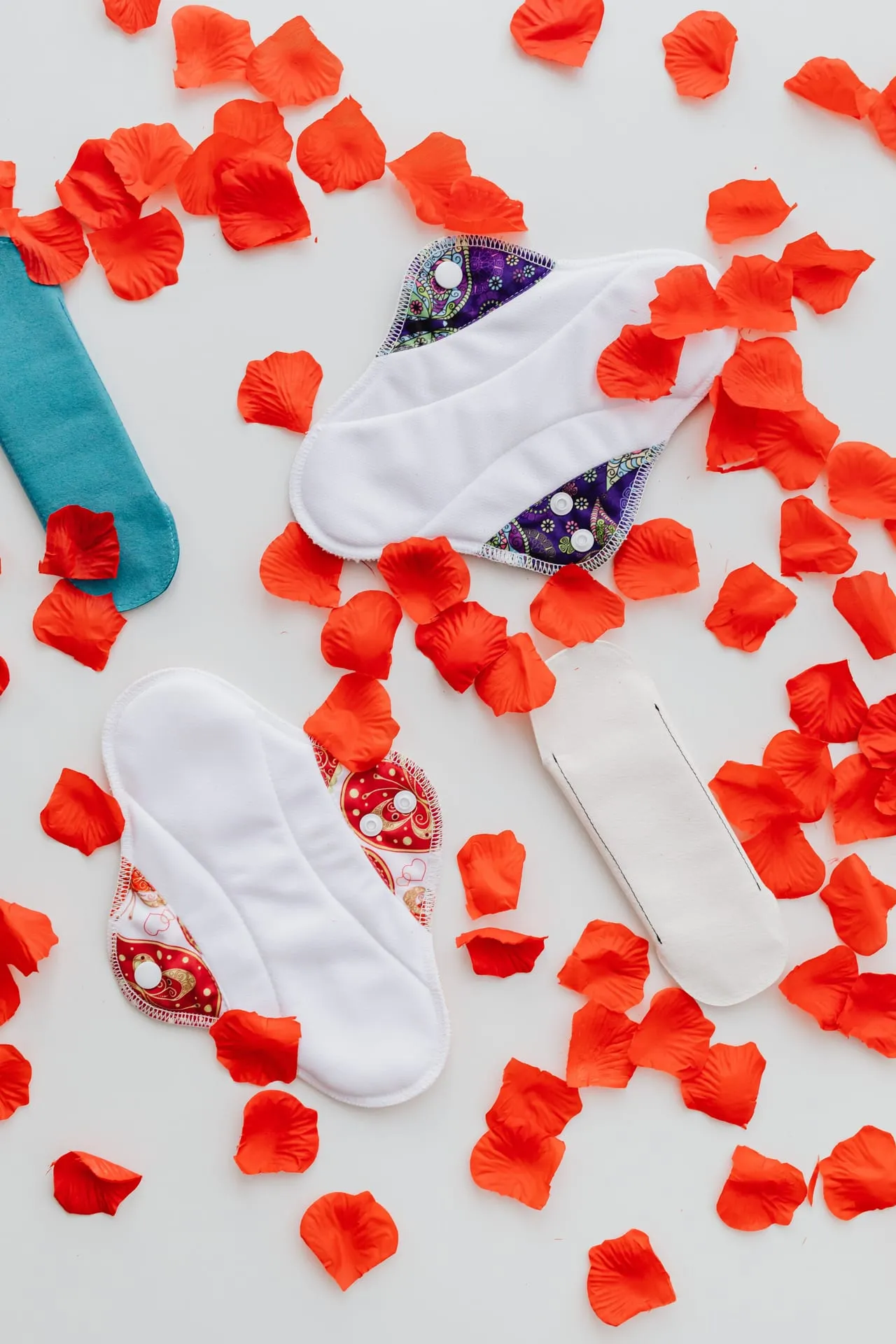 Reusable cloth sanitary pads laid out among red petals.