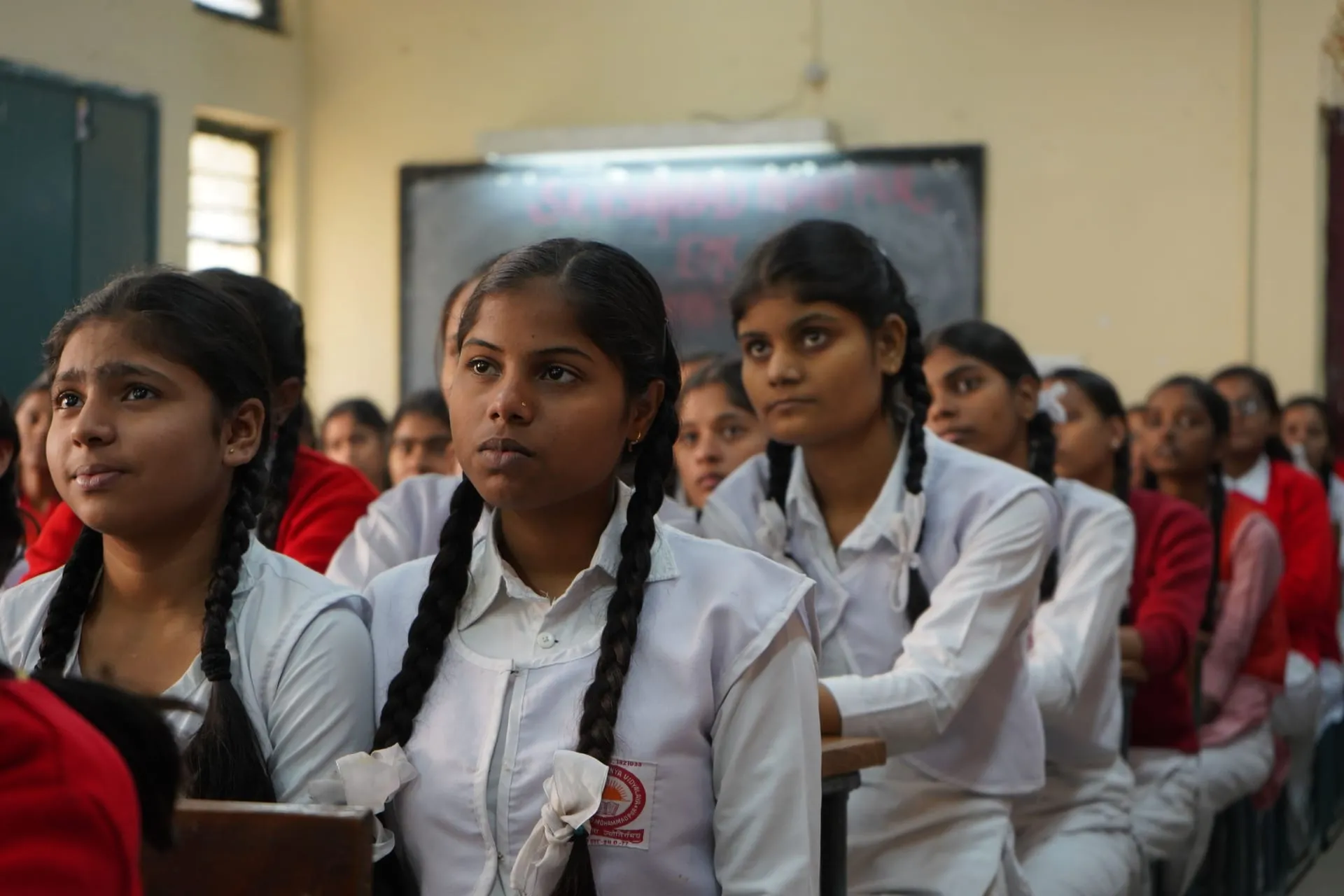 Schoolgirls in uniform sitting in rows in a classroom, listening closely.