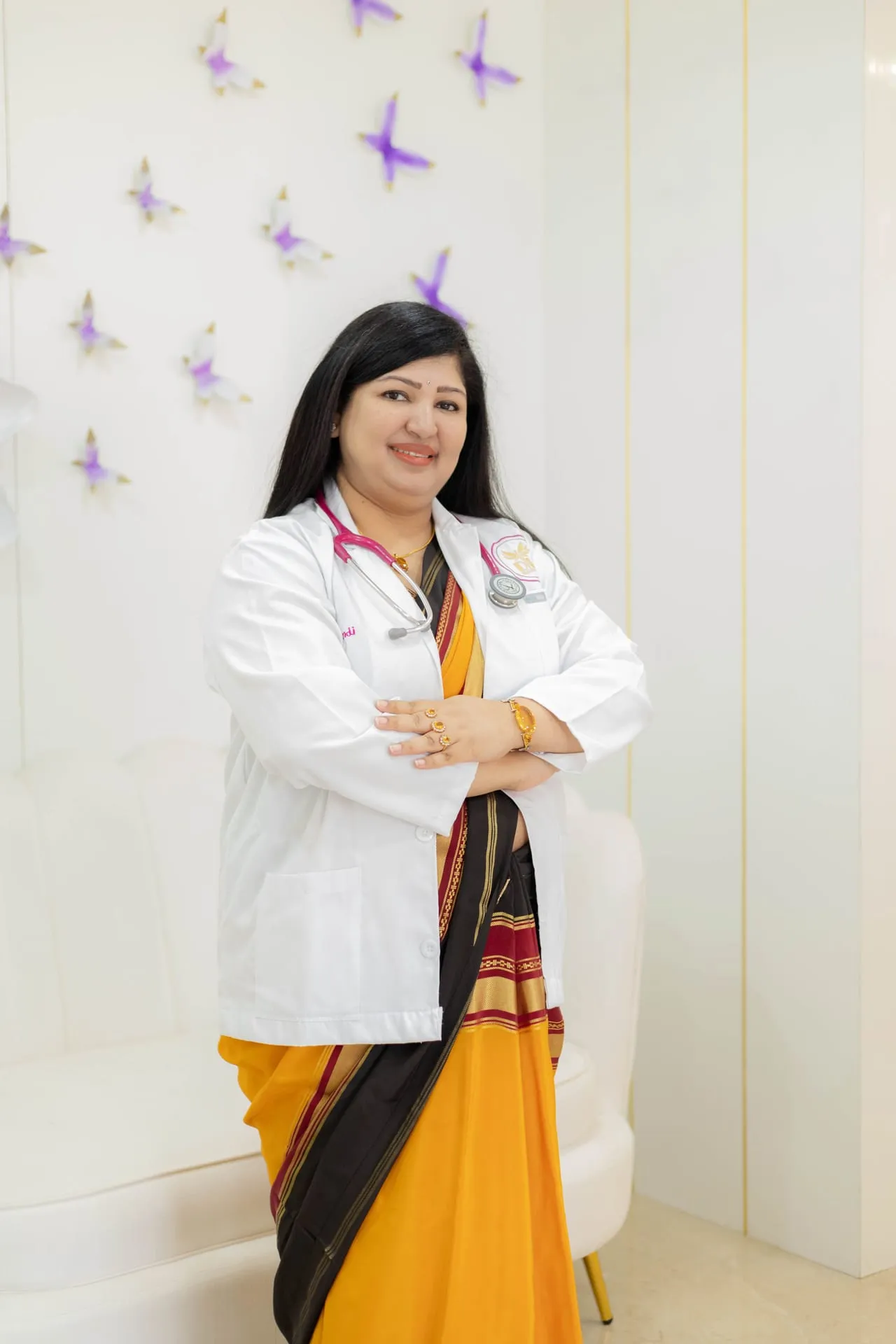 A smiling woman doctor in a sari and white coat, a stethoscope around her neck.
