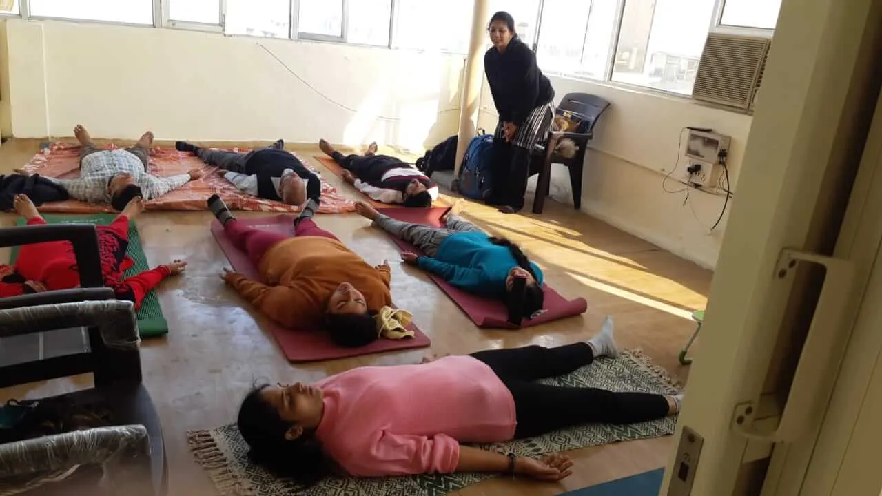 Participants resting flat on their mats while a teacher stands beside them.